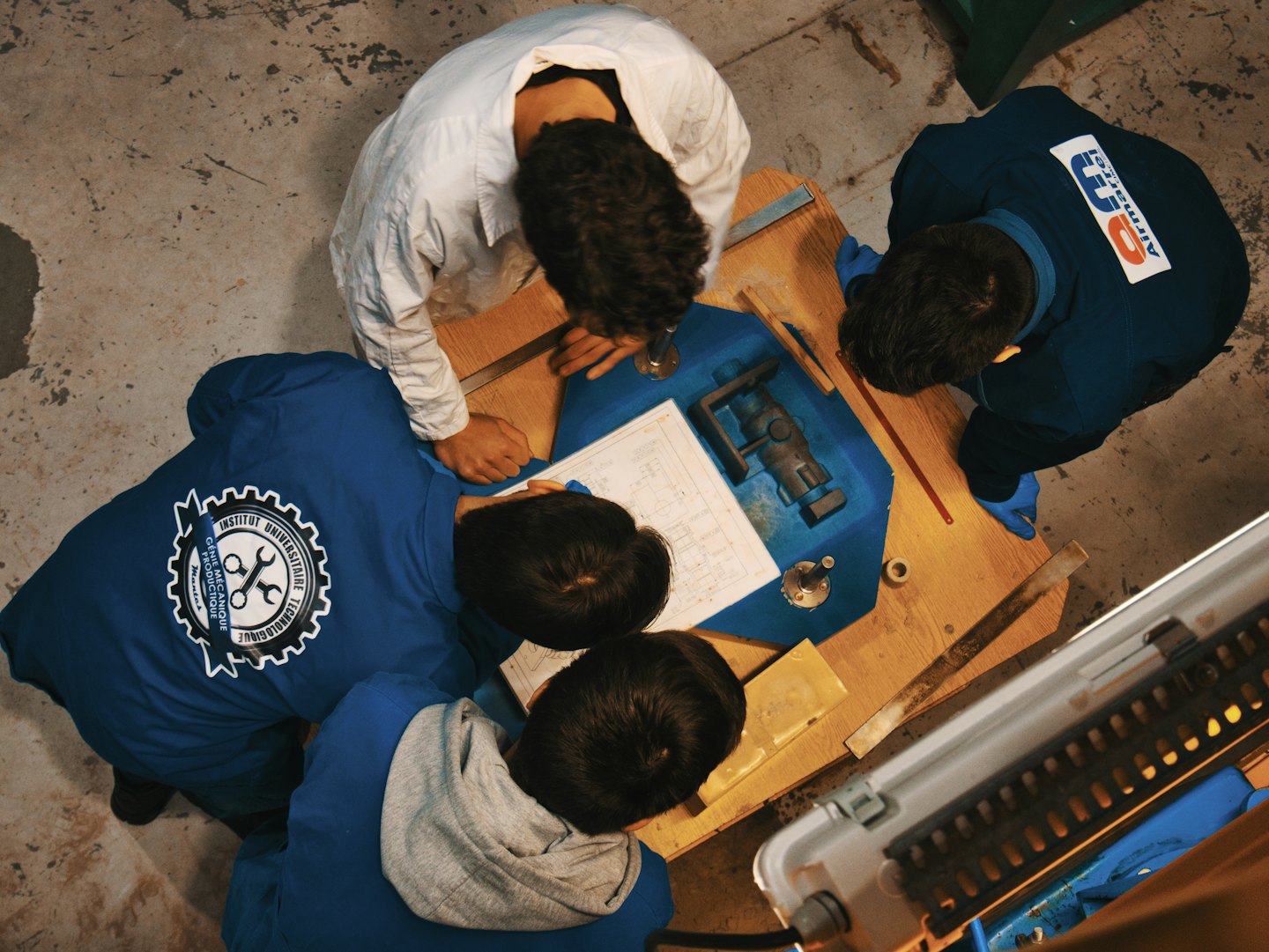 Quattro persone in divise da lavoro esaminano progetti su un banco da lavoro.