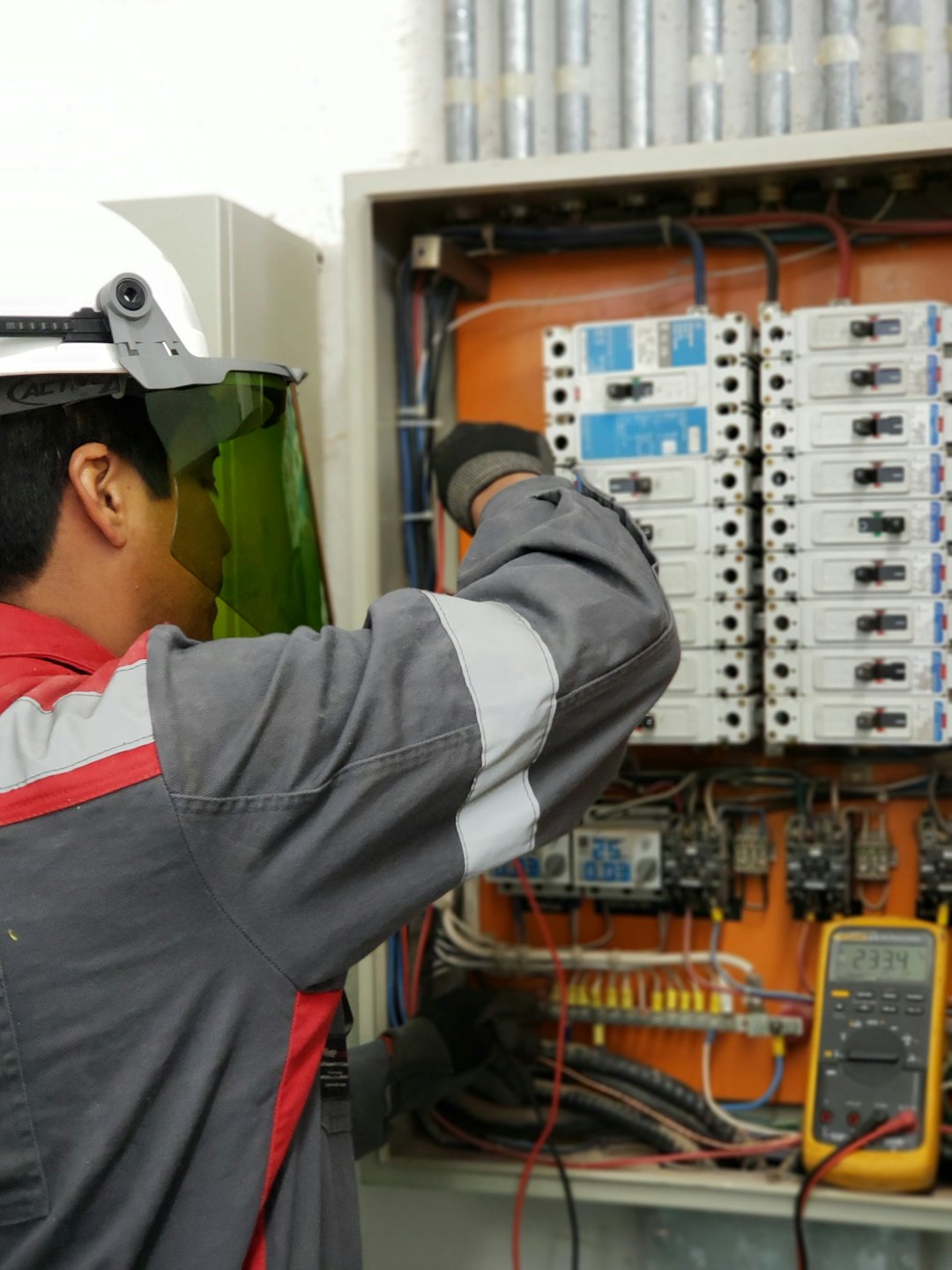 Tecnico ispeziona quadro elettrico aperto con interruttori e cavi.